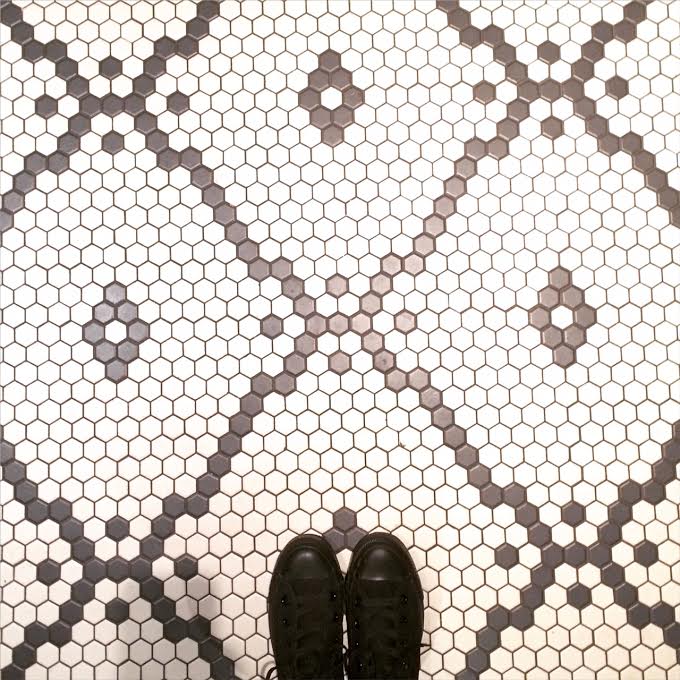 Looking down at a tile floor with a view of the tops of black Converse shoes