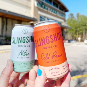 Nitro and Cold Brew Slingshot Coffee Co. cans held outside a Whole Foods Market
