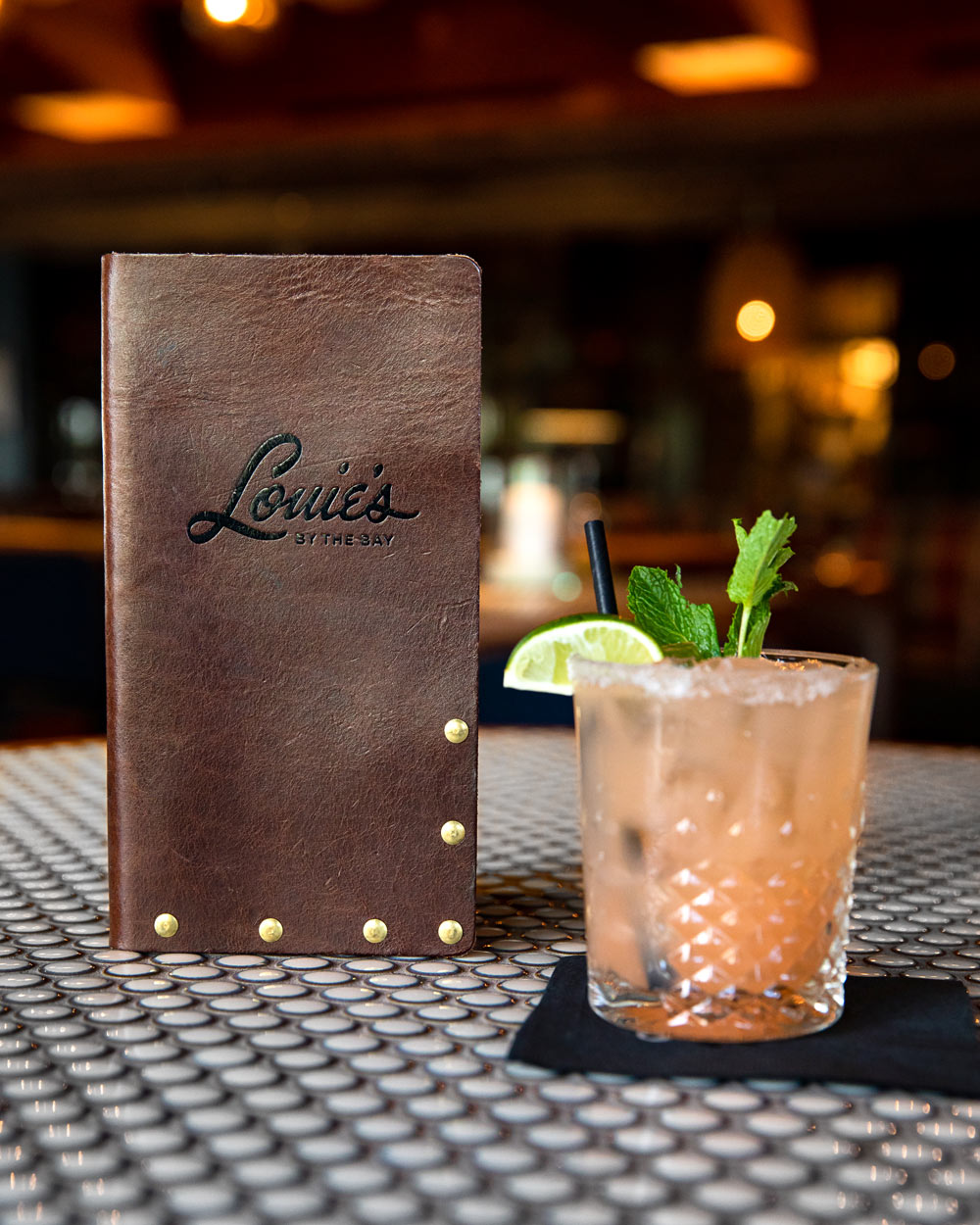 Leather Check Presenter with Louies By The Bay Restaurant Logo next to a mixed drink