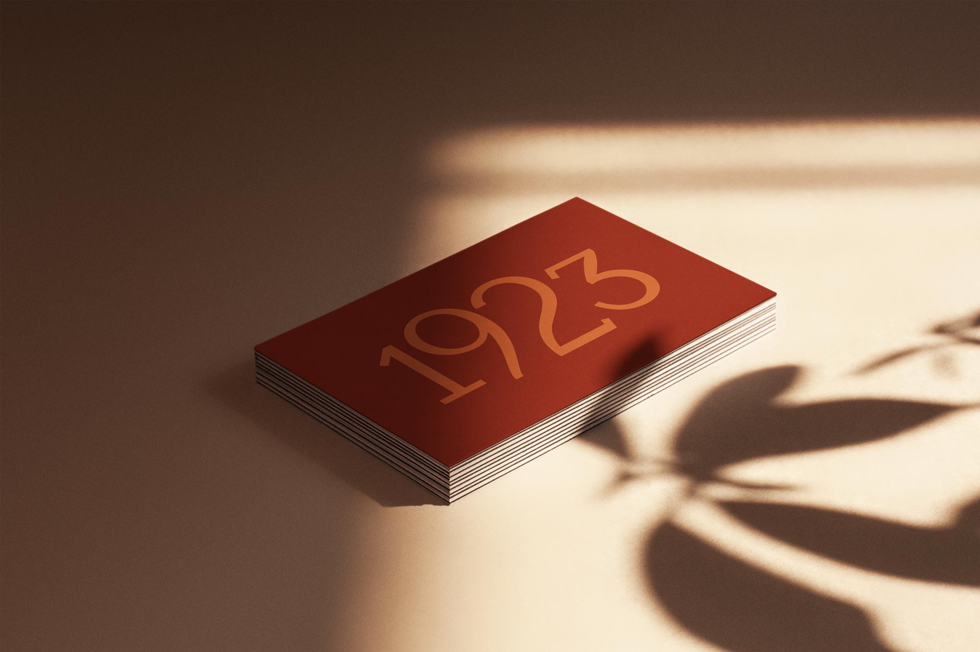 1923 Restaurant Group business card in red on a table with the shadow of a plant