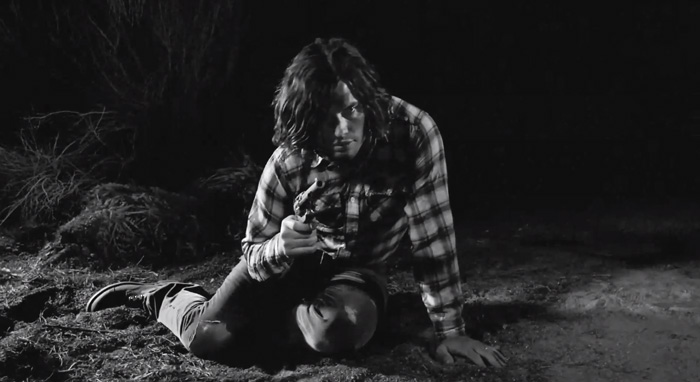 Josh Harmony music Video still frame of a guy holding a gun sitting on the dirt ground pointing the gun at the camera