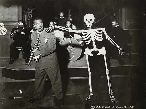Photo of a trumpet player in a band with a skeleton putting his hand on his shoulder