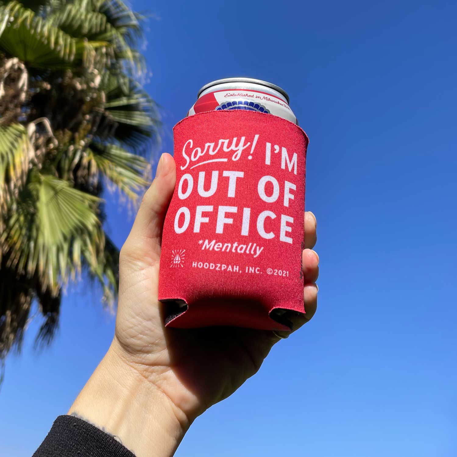 Out of Office Koozie by Hoodzpah in front of palm tree