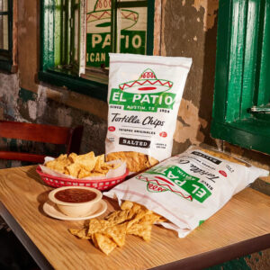 El Patio tortilla chip bag laying on a table slipping out with a cup of salsa